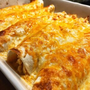 Creamy Sour Cream Chicken Enchiladas Ready in 45 Minutes 6 Close-up of baked Sour Cream Chicken Enchiladas topped with melted golden cheese in a white baking dish.