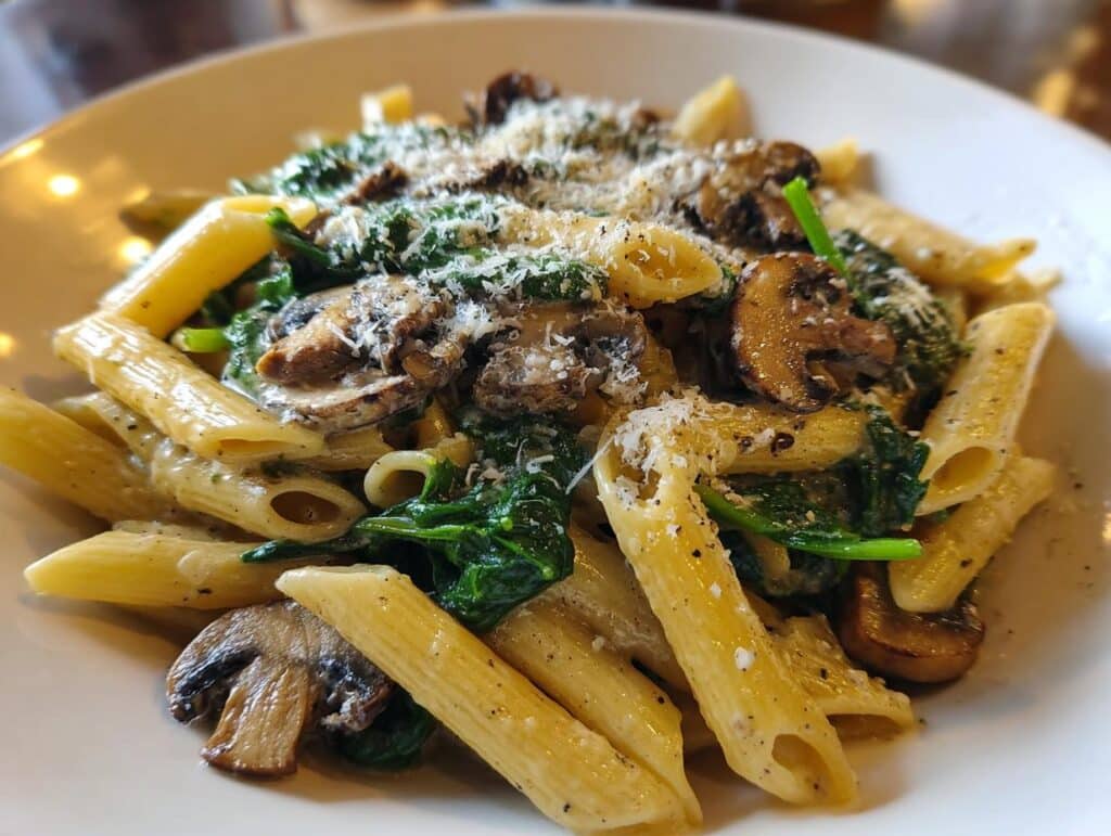 Close-up of a bowl of creamy Spinach and Mushroom Pasta, garnished with grated Parmesan cheese and black pepper.