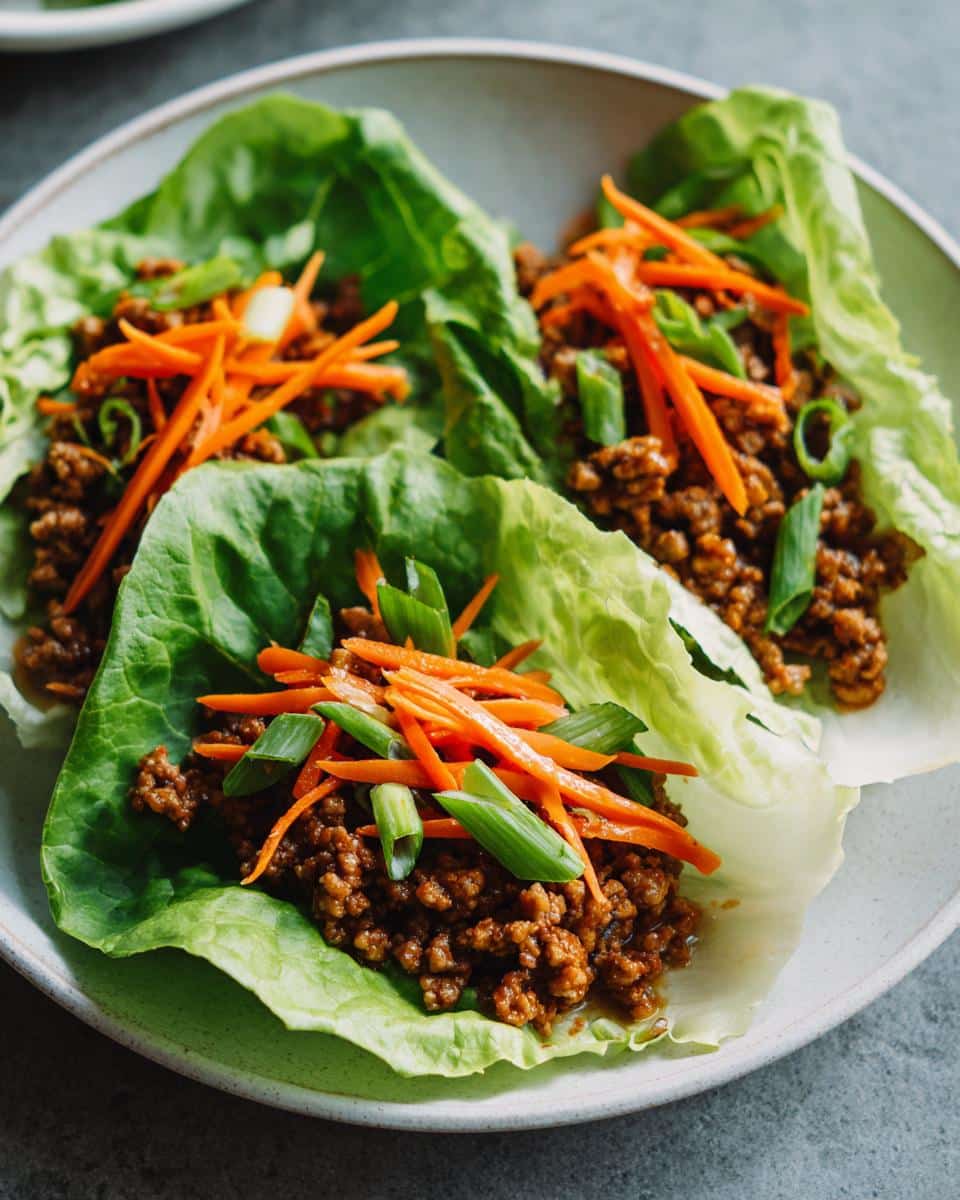Close-up of three vibrant Lettuce Wraps with Ground Turkey, topped with shredded carrots and green onions.