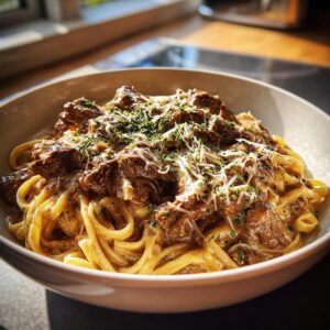 A close-up of a bowl filled with Creamy Garlic Beef Pasta, topped with grated cheese and fresh herbs.