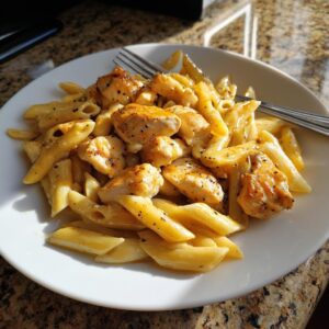 A close-up of a white plate filled with Creamy and Easy Garlic Butter Chicken Pasta, featuring penne pasta and chicken pieces.