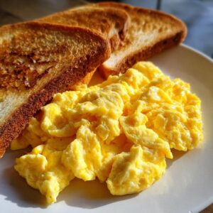 A plate of fluffy yellow scrambled eggs next to two slices of golden-brown toast, perfect for a Brunch Pin.