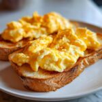 Close-up of two slices of toasted bread topped with fluffy scrambled eggs, lightly seasoned, ready for a delicious Brunch Pin.